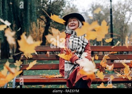 Happy blonde femme à la retraite assis sur un banc Banque D'Images