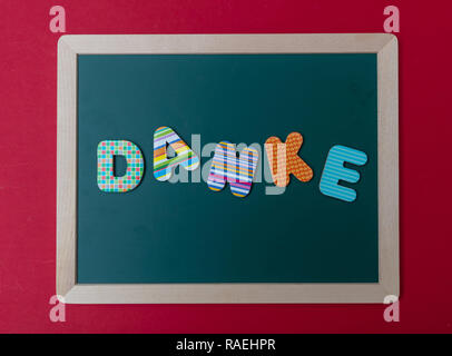 Danke, merci, lettres colorées en forme le mot Danke, merci en allemand, le conseil vert avec cadre en bois, red wall background Banque D'Images