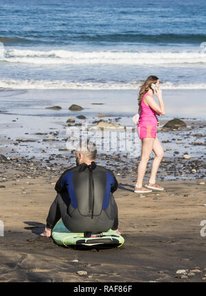 Surf mature sitting on surfboard on beach. Banque D'Images