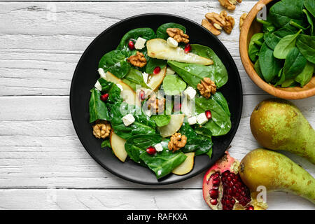 Salade de printemps frais avec les feuilles d'épinards, de poire, de noix, de grenade et le fromage feta en plaque noire. La nourriture végétarienne saine. Vue de dessus Banque D'Images