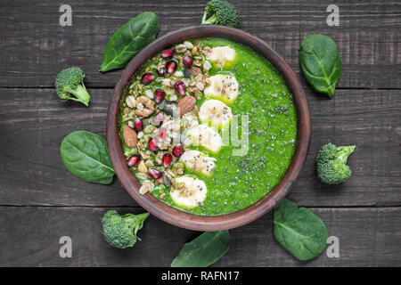 Les épinards et brocoli vert sain bol smoothie banane garnie de granola., grenade et chia seeds sur fond de bois foncé, en bonne santé vue d'en haut. Banque D'Images