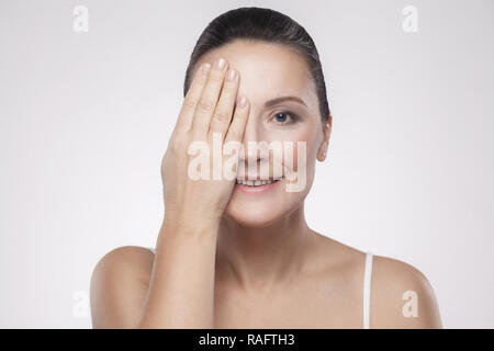 Closeup portrait of happy smiling dentelée charmant, beau, jolie femme d'âge moyen avec la peau du visage parfait se cache un oeil avec la main isolé sur gre Banque D'Images