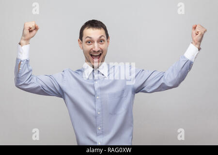 Portrait d'homme en soie beau joyeux excité dans classic light blue shirt debout avec les bras levés et de célébrer sa victoire. Piscine stud Banque D'Images