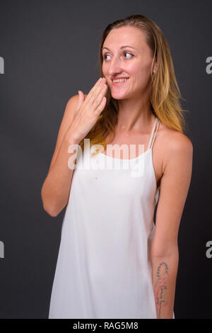 Belle jeune femme aux cheveux blonds tout droit contre le dos gris Banque D'Images