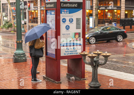 Une femme sous parapluie est de vérifier le MAX Light Rail annexe à la gare dans le centre-ville de Portland, Oregon, USA Banque D'Images