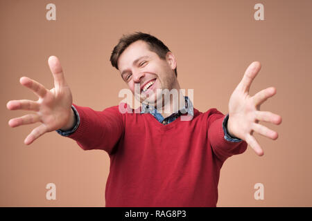 Bienvenue, content de vous voir. Man in red sweater looking at camera avec les bras levés et de bonheur. Banque D'Images