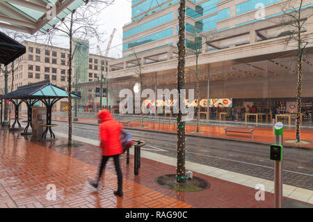 Un piéton marche sur le trottoir pendant la pluie, avec l'Apple Store en arrière-plan, le centre-ville de Portland, Oregon, United States. Banque D'Images