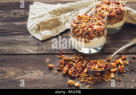 Granola fait maison, du muesli avec des écrous et des canneberges séchées et yogourt en verres sur fond de bois rustique. Petit déjeuner sain. Banque D'Images