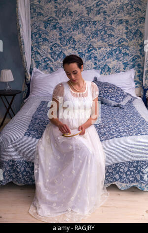 Attractive young woman in dress regency authentique assis sur un lit d'époque Banque D'Images