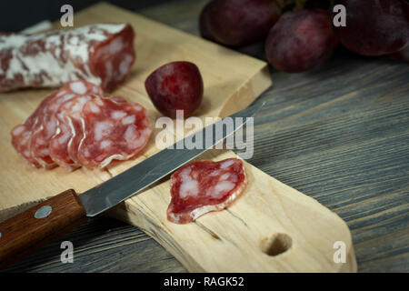 Tranches de salami et de raisin rouge sur la planche à découper en bois avec couteau Banque D'Images