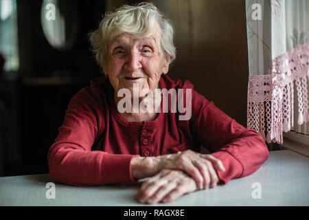 Les émotions d'une femme âgée assise à la table. 90 ans. Banque D'Images