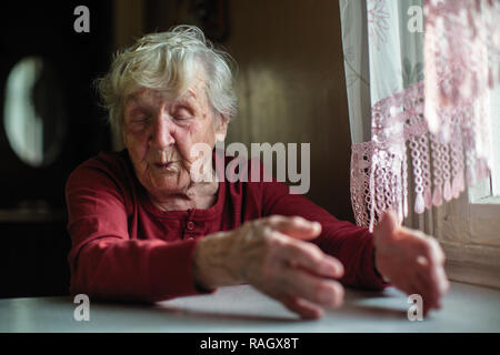 Les émotions d'une femme âgée assise à la table. 90 ans. Banque D'Images
