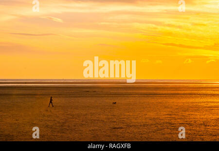 Walker et le chien sur la plage au coucher du soleil en hiver à la recherche sur la rivière Ribble estuary à Lytham St Annes Lancashire England UK Banque D'Images