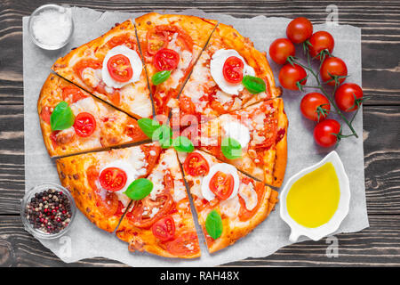 Des tranches de pizza Margherita avec tomates, basilic, romarin et de mozzarella sur fond de bois rustique. Vue de dessus Banque D'Images