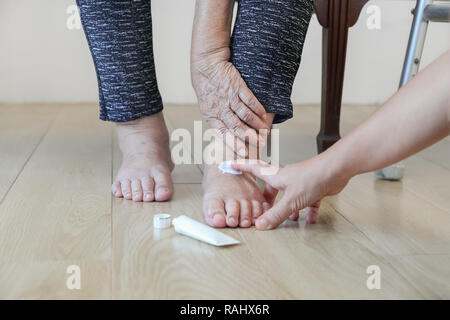 Femme âgée de mettre de la crème sur les pieds enflés Banque D'Images