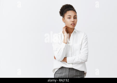 Désolés Qu'est-ce que vous parlez. Portrait de femme avec l'espacement des pensées en discutant de quelque chose avec un collègue, regardant avec expression rêveuse et toucher le cou tout en pensant au mur gris Banque D'Images