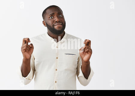 L'homme préoccupé par faire face, croisant les doigts, espérant pour de bons résultats. Portrait de beau nerveux à la peau sombre moderne entrepreneur, mordre la lèvre, le fixant, avec anxiété, appareil photo, priant ou décisions tiens Banque D'Images