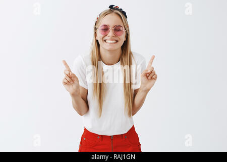 Quel plaisir d'être numéro un. Portrait d'optimiste souriant et espiègle jeune femme blonde à lunettes et serre-tête, souriant joyeusement, se pencher vers la caméra avec les doigts levés et sourire pur Banque D'Images