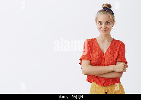 Taille plan sur certain blonde féminine en rouge de style vintage et vêtements à pois holding bandeau mains croisées sur la poitrine et souriant de l'auto-assurance et l'expression heureuse Banque D'Images