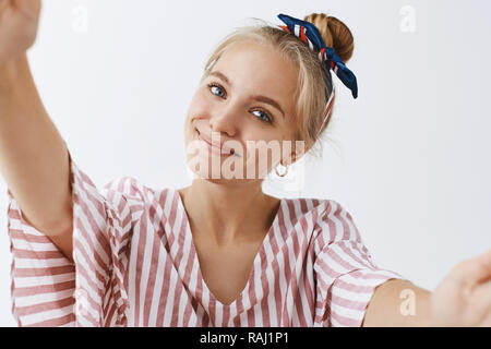 Femme parlant avec copain via la vidéo en ligne, levage smartphone pour danser ou faire. selfies Charmant et très mignon femme blonde dans un bandeau et un chemisier, tilting head et souriante, appareil photo touchante Banque D'Images