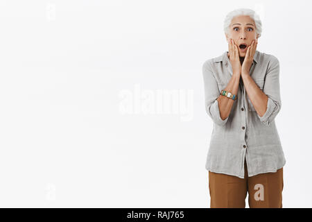 Portrait de choqué et excité senior lady avec chute de cheveux blancs jaw toucher le visage avec les deux paumes réagissant sur scène choquante et terrifiantes images sur fond gris Banque D'Images