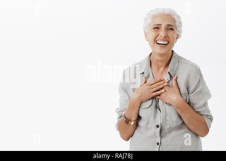 Vieille Femme insouciante heureux satisfait de comment va la vie. La haute dame charmante joyeuse avec des cheveux gris en chemise holding palms sur la poitrine et impression de rire amusé à parler avec les petits-enfants Banque D'Images