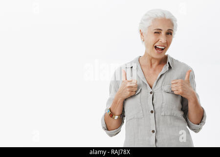 Les personnes âgées peuvent rock aussi. Charmant Portrait de mamie enthousiaste avec les cheveux gris en chemise showing Thumbs up en geste comme un clin et contemplant l'approbation de l'appareil photo idée impressionnante Banque D'Images