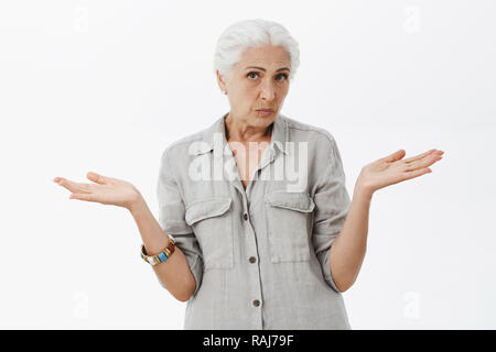 Taille plan sur clueless incertain granny mignon avec des cheveux blancs en haussant les mains avec propagation de côté et pas au courant ce qui se passe en essayant de trouver des réponses sur fond gris Banque D'Images