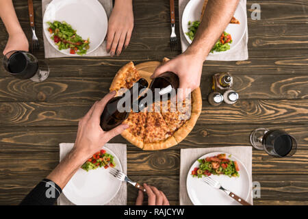 Portrait de friends toasting tout en dînant avec des pizzas et des salades à table en bois Banque D'Images