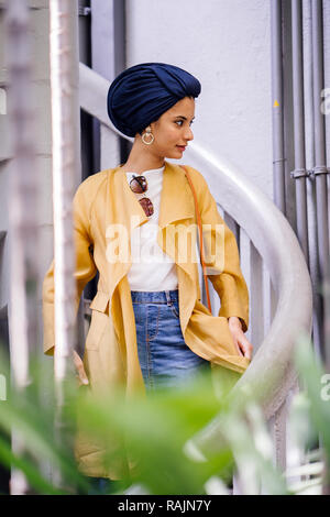 Fashion portrait d'une jeune et belle femme du Moyen-Orient arabe dans un élégant costume pastel et turban hijab debout sur un escalier en spirale. Banque D'Images