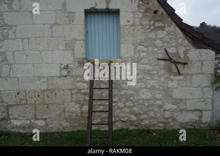 L'ancienne échelle de bois appuyé contre le mur en pierre calcaire d'une maison typique dans la vallée de la Loire, France avec des volets verts sur une fenêtre Banque D'Images