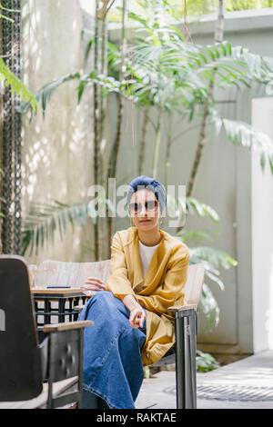 Fashion portrait d'une jeune et belle femme asiatique malais (musulmans) dans un turban et lunettes de soleil. Elle est de vous détendre dans un café branché. Banque D'Images