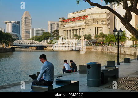 Les gens se détendre au bord de la rivière Singapour près de Boat Quay, en arrière-plan Pont Cavenagh et Fullerton Hotel (à droite) Banque D'Images