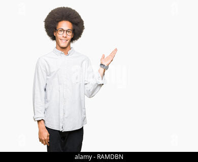 Young african american man with afro hair portant des lunettes smiling cheerful présentant et en pointant avec la paume de la main regardant la caméra. Banque D'Images