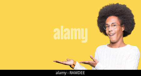 Young african american man with afro hair portant des lunettes en pointant sur le côté avec la main et ouvrez Palm, la présentation de votre annonce en souriant heureux et confiant Banque D'Images