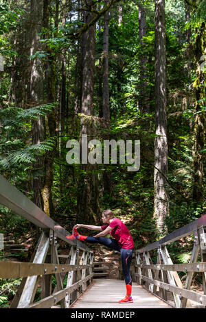 Fille étirant des hamstrings dans le pont à l'intérieur de la forêt de Deep Cove au Canada Banque D'Images