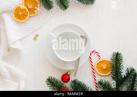 Composition de Noël avec des décorations. Tasse blanche vide, en écharpe et branches de sapin sur une table en bois blanc avant la veille de Noël. Banque D'Images