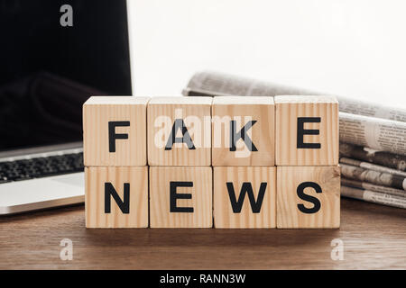 Cubes en bois avec des mots faux news, ordinateur portable et de journaux sur la table en bois Banque D'Images