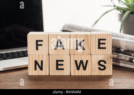 Cubes en bois avec des mots faux news, usine, ordinateur portable et de journaux sur la table en bois Banque D'Images