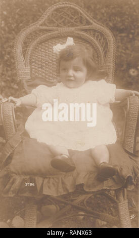 Vintage Carte postale photographique d'un enfant assis dans un fauteuil en osier dans le jardin Banque D'Images