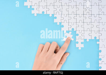 Vue partielle de la femme avec des morceaux de puzzles blanc sur fond bleu Banque D'Images