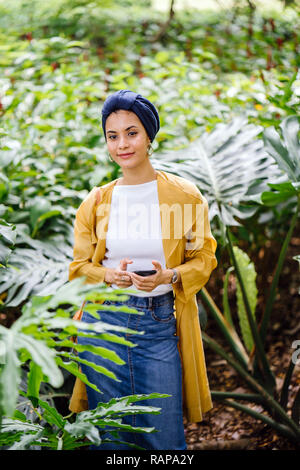 Portrait d'une jeune, jolie et belle femme musulmane d'Asie malais dans un turban hijab foulard debout dans un parc et à l'aide de son smartphone. Banque D'Images