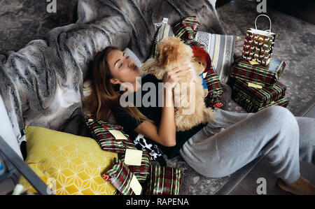 Embrassant son animal de dame cutie puppy red avec curly. Allongé sur un canapé entre présente de ses amis et de sa famille. Jouer et avoir du plaisir ensemble. L'hiver, Banque D'Images