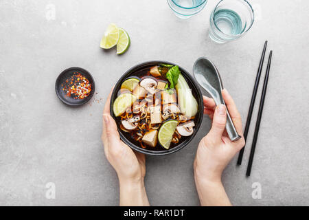 Jeune femme manger asiatique savoureux potage végétarien ou végétalien servi dans un bol noir sur gris table. Vue de dessus. L'horizontale. Banque D'Images