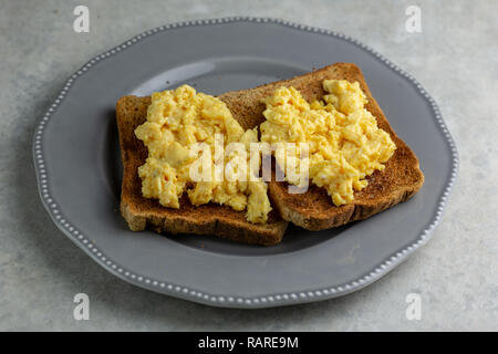 Oeufs brouillés sur deux morceaux de pain grillé sur une plaque gris sur un simple fond marbré gris et blanc Banque D'Images