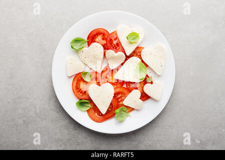 Valentines Day salade. Salade caprese classique italien avec coeur formé de la mozzarella, tomates et basilic servi sur assiette. Vue ci-dessus. Copier l'espace. Banque D'Images