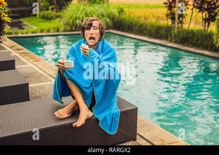 Homme malade de voyageur. L'homme a attrapé un rhume en vacances, se trouve triste à la piscine, boire du thé et souffle son nez dans un linge. Son fils est en bonne santé et la natation dans la piscine. Billet d'avion concept Banque D'Images