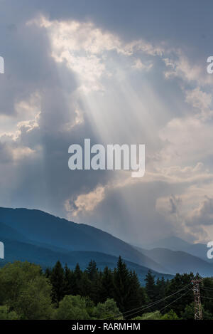 Les rayons du soleil font leur chemin à travers le ciel d'orage dans les sommets des montagnes Banque D'Images