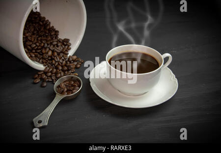 Tasse de café fumante dans la porcelaine blanche tasse et soucoupe sur les grains de café dans un récipient. Banque D'Images