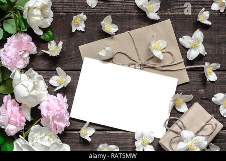 Carte de voeux blanche rose et blanc avec roses dans cadre fait de fleurs de jasmin avec boîte-cadeau sur une table en bois rustique. Télévision. Vue de dessus Banque D'Images